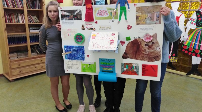 Grupa uczniów na korytarzu szkolnym prezentuje pracę konkursową: lapbook "Moja szkoła marzeń".