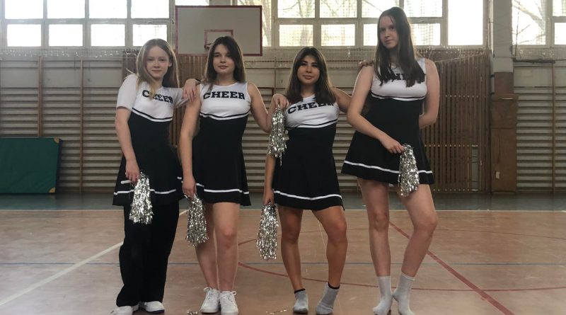 W sali gimnastycznej stoją cztery dziewczynki w biało czarnych strojach cheerleaderek.
