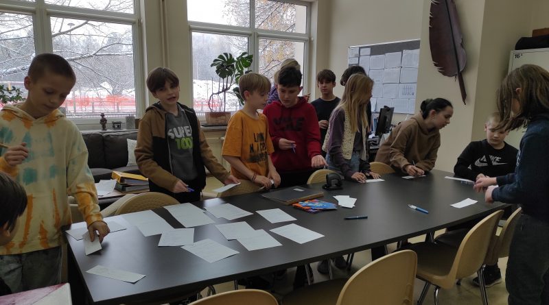 Duży stół, na nim kartki, wokół stołu uczniowie biorący udział w głosowaniu.