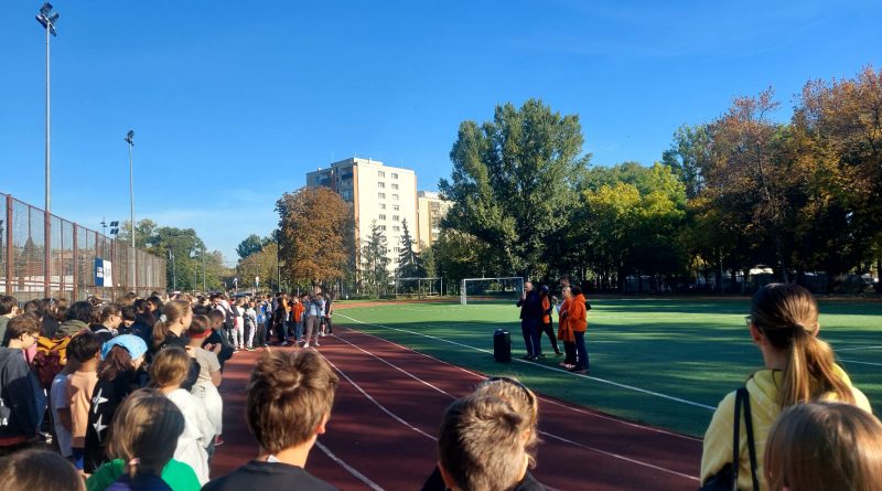 Boisko szkolne, po lewej stronie uczniowie, na środku kilkoro dorosłych obok głośnika.
